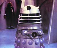 Image of a Dalek, with The Doctor restrained in the background
